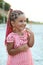 Cute little tanned girl with colored braids hairdo wearing a pink dress is very curious at the summer beach