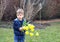 Cute little thoughtful boy in blue vest holding bouquet of bright yellow daffodils flowers staying in spring park
