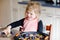 Cute little toddler girl baking plum pie at home. Happy smiling child helping and preparing plums for cake in domestic