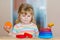 Cute little toddler girl playing alone with colorful wooden rainbow pyramid and toys at home or nursery. Happy healthy