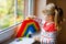 Cute little toddler girl by window create rainbow with colorful plastic blocks. People with rainbows around the world as