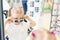 Cute little young caucasian blond girl trying on and choosing sunglasses in front of mirror at optic eyewear store. Adorable