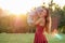 Cute long-haired tanned woman enigmatic smile in a red dress tosses throws a gray teddy bear toy in hands in the park