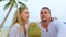 Cute loving couple facing each other sits in tropical beach under palm tree and drink coconat cocktail, laugh and having