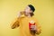 Cute man in a cap isolated on a yellow background with a burger in his hands, starving staring at fast food