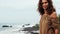 Cute mature woman with brown curly hair stands at cliff and stares at sea waves