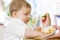 Cute messy baby boy playing with food while eating.