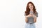 Cute modern millennial girl with red curly hairstyle, tilt head joyfully, smiling enthusiastic, holding smartphone