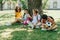 Cute multicultural schoolkids talking while sitting on lawn under tree