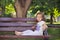 Cute musical baby child girl with brunette hairs and stylish wear enjoying life sitting on wooden chair bench in summer awesome pa