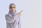 Cute Muslim woman with cheerful face expression points away with her forefinger, showing to copy space on the corner. Portrait of