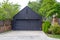 Cute neat shingled garage and driveway with landscaping and green trees