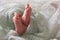 Cute newborn baby covered in turquoise crocheted plaid on bed, closeup of legs