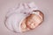 Cute newborn baby girl with a bow on her head sleeping on a pink