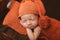 Cute newborn baby in hat on a brown bed and orange pillow . Sleeping baby on a dark background. Closeup portrait of newborn baby.