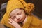 Cute newborn baby in hat on a brown bed and yellow pillow . Sleeping baby on a dark background. Closeup portrait of newborn baby.