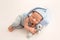 A cute newborn boy in the first days of life sleeps in a blue overalls a background of white fabric.