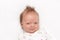 Cute newborn is smirking on the white carpet. Adorable baby boy looking at camera