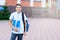 Cute, nice, young 11 years old boy in blue shirt stands with workbooks and backpack in front of his school. Education