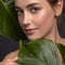 Cute ordinary young woman posing with monstera tropical leafs. Fresh clean skin with flawless texture. Skin care beauty