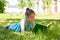 Cute pensive little girl lying on a green grass in summer park and reading a book