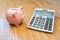 Cute Piggybank and calculator on wooden background