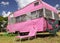 Cute pink travel trailer under a bright cloudy sky with cacti and trees around a tumbona chair