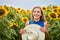 A cute pleasant woman smiles and holds a hat against a background of yellow sunflowers. Walks in the open air