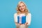 Cute positive blond woman in knitted sweater holding in hands blue giftbox with ribbon bow, making present, surprise