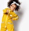 Cute positive curly mulatto african girl in warm yellow sports jumpsuit and hair bow showing thumb up sign with fingers