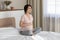 Cute pregnant woman laughing sitting on king size bed