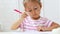 Cute preschool girl sitting by the white table focused on drawing something.