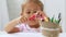 Cute preschool girl sitting by the white table focused on drawing something.