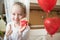 Cute preschooler girl celebrating 6th birthday. Girl eating her birthday cupcake in the kitchen, surrounded by balloons.