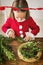 Cute preschooler girl dressed in reindeer costume wearing reindeer antlers making christmas wreath in living room.