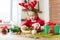 Cute preschooler girl dressed in reindeer costume wearing reindeer antlers making christmas wreath in living room.