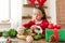 Cute preschooler girl dressed in reindeer costume wearing reindeer antlers making christmas wreath in living room. Christmas decor