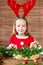 Cute preschooler girl dressed in reindeer costume wearing reindeer antlers making christmas wreath in living room. DIY Christmas.