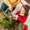 Cute preschooler girl wearing reindeer antlers and her mother making christmas wreath in living room. Christmas family fun.