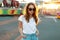 Cute pretty stylish hipster young woman in vintage jeans in fashionable sunglasses in a white stylish t-shirt walks