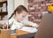 Cute pretty young girl doing complex maths writing calculations at home school with computer laptop and calculator on colourful