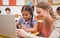 Cute pupil using computer with teacher