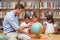 Cute pupils and teacher looking at globe in library