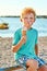 Cute red curly boy is extremely happy while getting dirty and eating ice cream on the summer beach