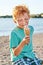 Cute red curly boy is extremely happy while getting dirty and eating ice cream on the summer beach