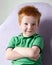 Cute red haired freckled little boy in green t-shirt waiting for doctor in medical office