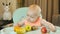 Cute red-haired girl in a high chair tastes fruits. Adorable child tasting fruits. Children\'s breakfast with fresh