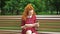 Cute red haired girl reading funny book in park