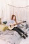 Cute red-haired woman learns to play the guitar, sitting on the bed, in a room in the style of boho