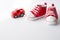 Cute red small sized canvas shoes with toy car top view on white background . copyspace